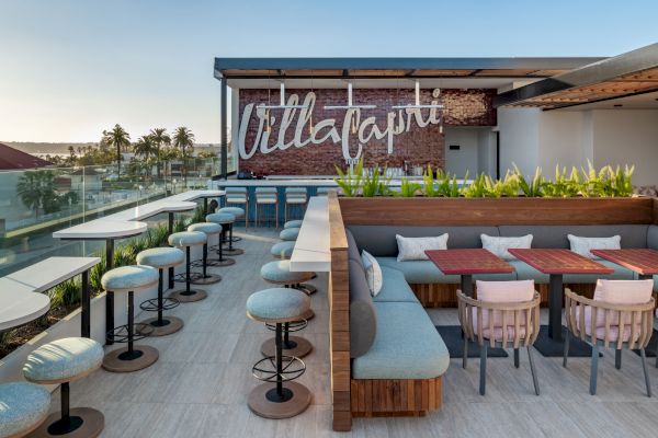 Rooftop terrace with stylish seating, tables, and a sign reading "Villa Capri." Scenic views and greenery create a welcoming atmosphere.