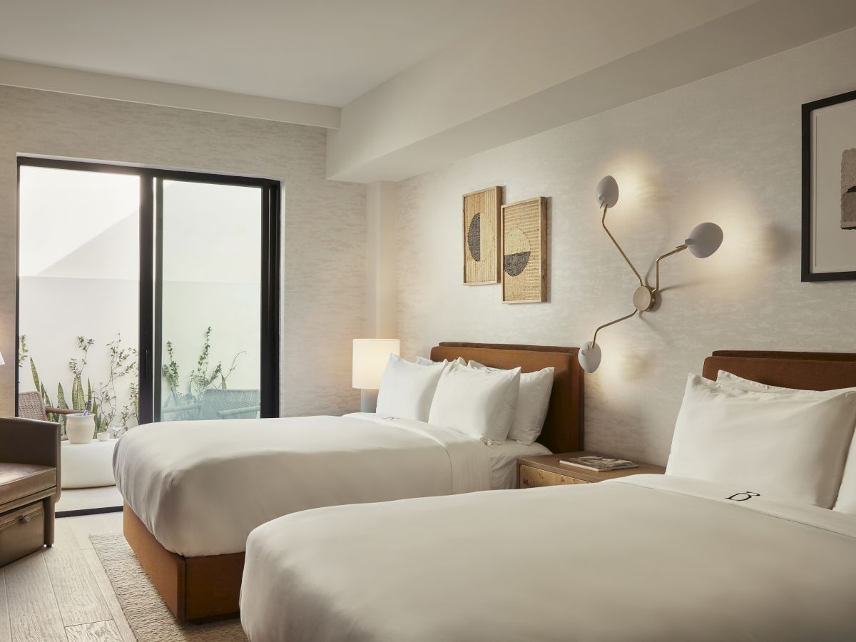 A modern hotel room with two beds, a contemporary lamp, and framed artwork. There's a seating area and a balcony with a view outside.