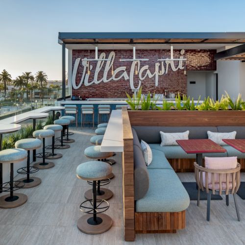 The image shows a stylish outdoor rooftop seating area with tables, chairs, and a sign on a brick wall.
