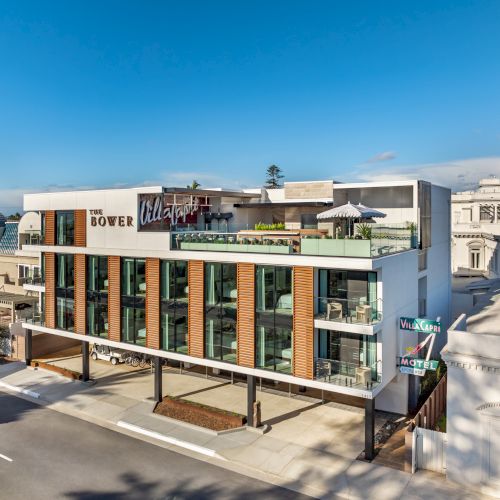 A modern three-story building with a rooftop area, featuring a restaurant named "The Rooftop." The street is quiet and the sky is clear.
