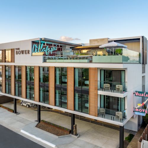 The image shows a modern building with signs for "The Dover" and "Villa Capri Motel," featuring balconies and a rooftop area with a parasol.