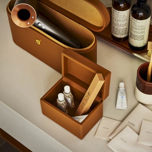 A bathroom counter with toiletries, a hairdryer in a leather case, a toothbrush, and personal care items arranged neatly.