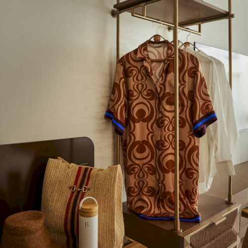 Clothes hanging on a rack with a patterned shirt, hat, water bottle, and bag in a neatly arranged setting.