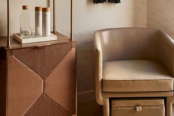 The image shows a beige leather chair and a wooden cabinet with glass bottles and cups on a tray.