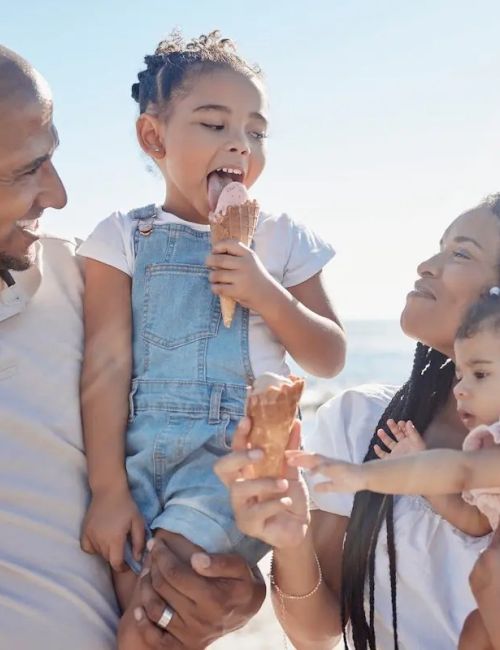A family enjoys ice cream together outdoors, with a bright clear sky in the background.