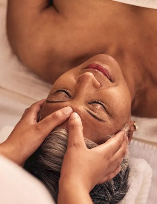 A person is receiving a relaxing face massage while lying down on a white towel, showcasing a calming spa environment.