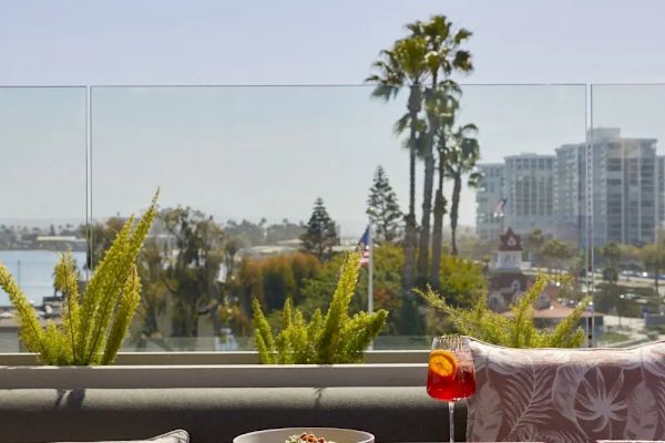 Open-air dining setup with a shaded table, plants, and city view with palm trees and buildings in the background.