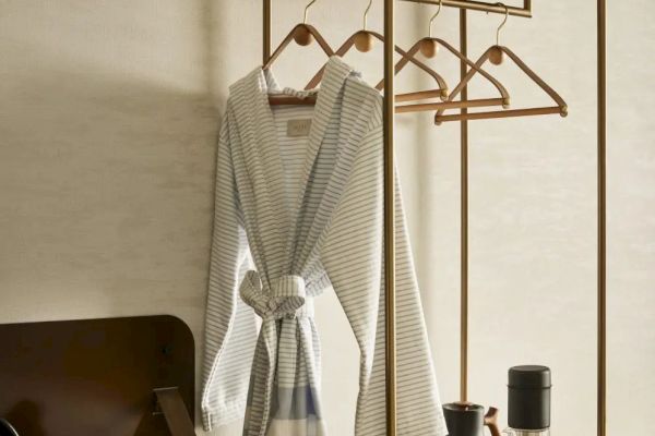 A room with a robe, hangers, a suitcase, and a shelf with plants and coffee items on a small cabinet.